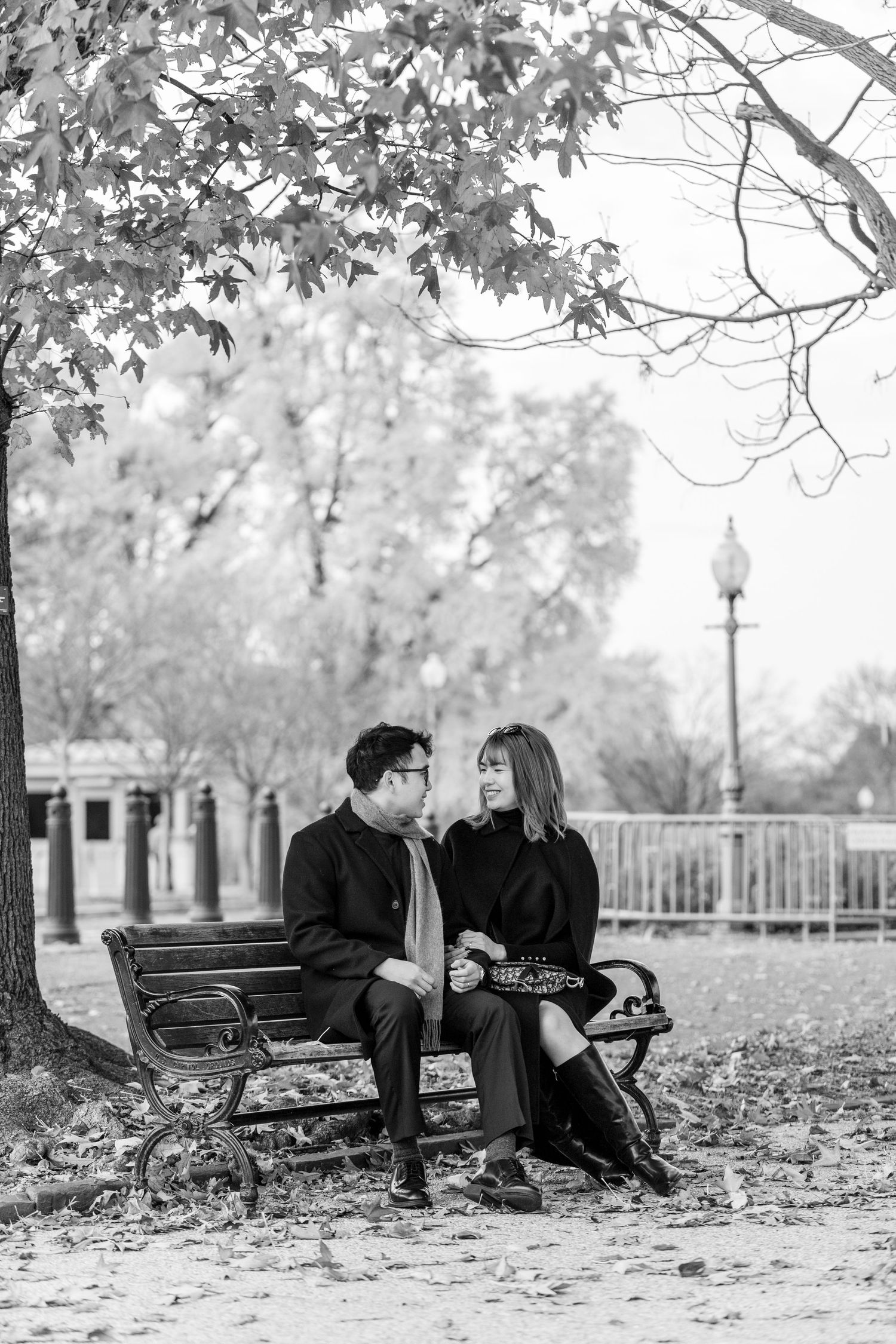 Romantic autumn engagement photos on park bench surrounded by fallen leaves.