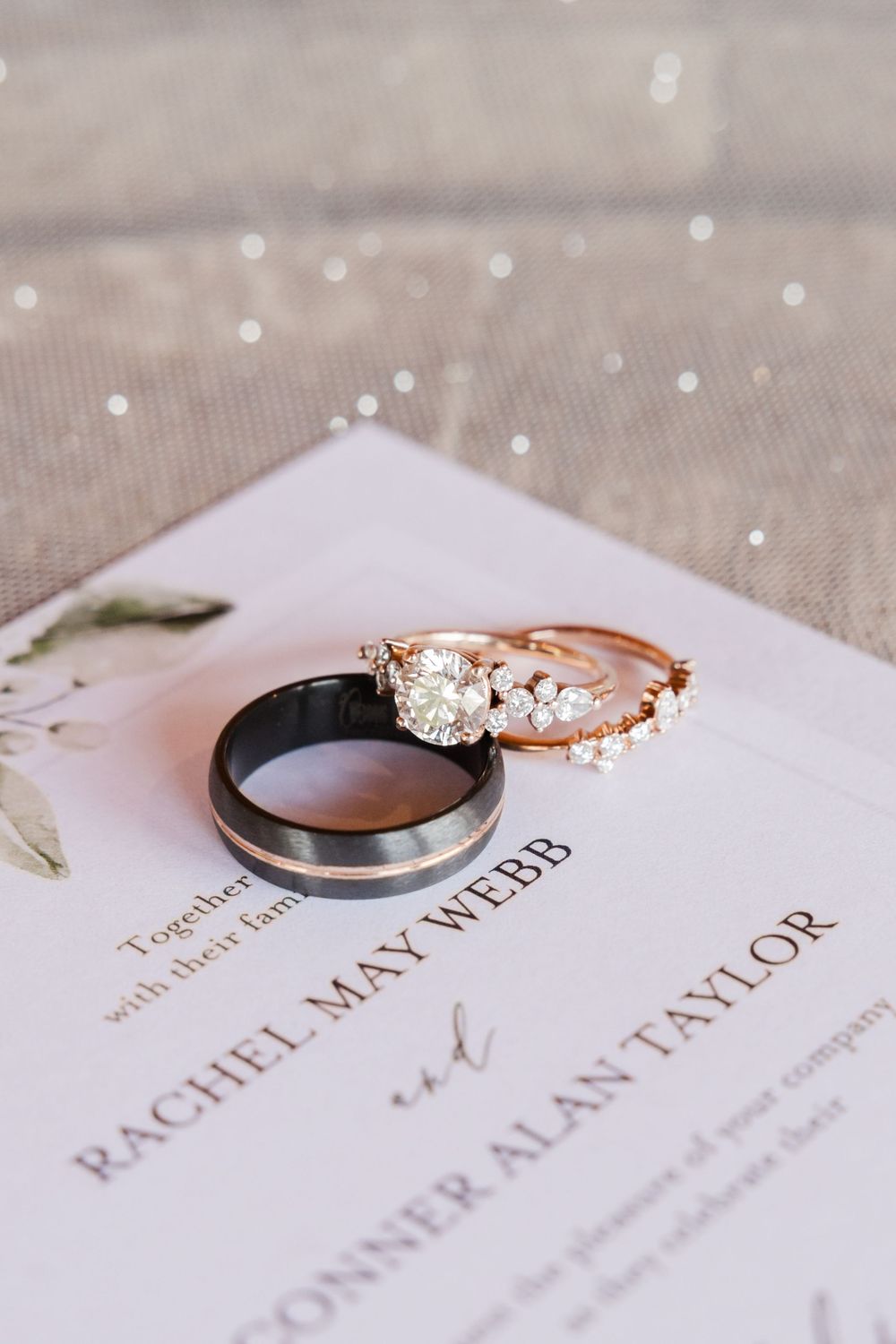 Wedding rings and invitation details laid out on a textured linen background with delicate lighting.