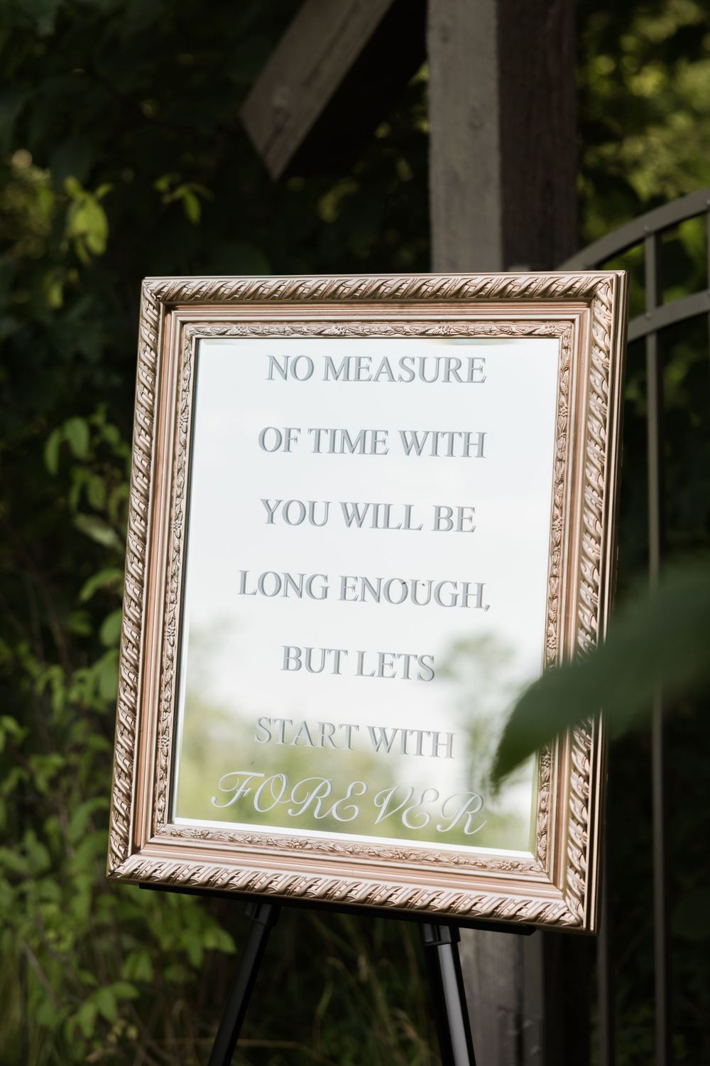 Framed wedding signs with romantic quotes displayed in ornate gold frames against a natural outdoor backdrop.