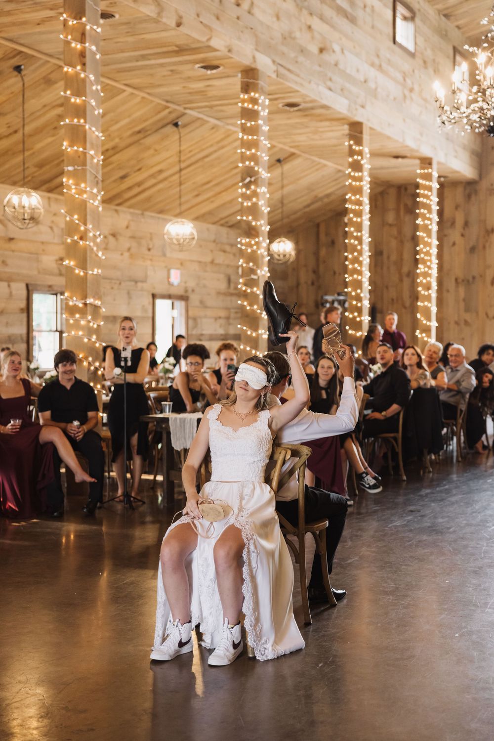 Wedding ceremony in a rustic barn with string lights and guests seated in rows.