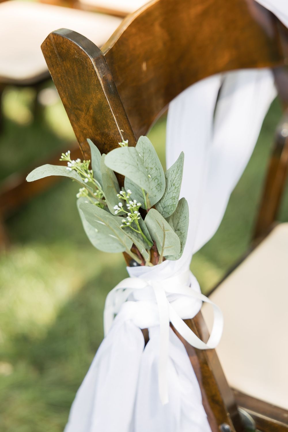 White ribbons and eucalyptus decorate wooden ceremony chairs along the aisle.