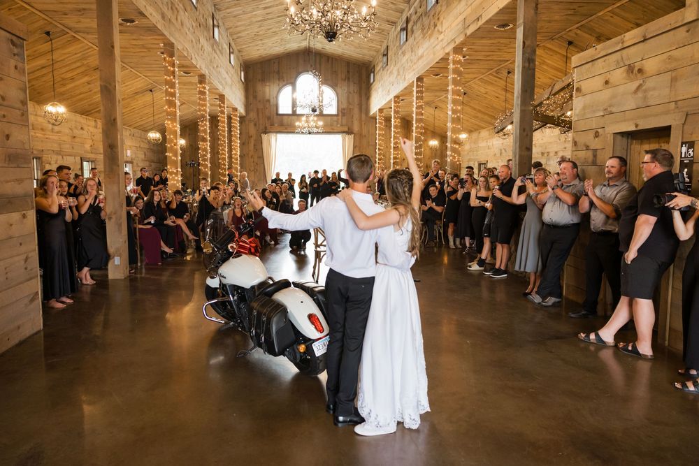 Couple performs their first dance in a rustic wooden barn venue with chandelier lighting and guests watching from the sides.