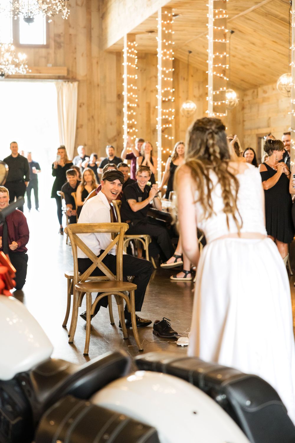 Wedding ceremony in a rustic barn venue with string lights and wooden chairs arranged for guests.