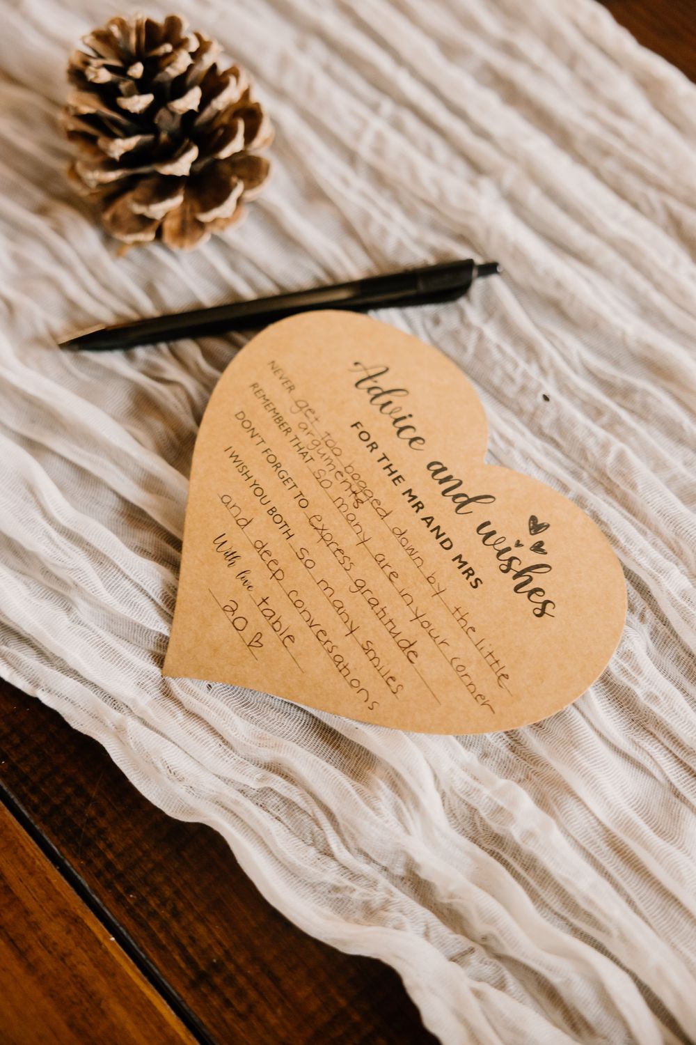 Heart-shaped wedding vows card displayed with pinecones on white fabric.