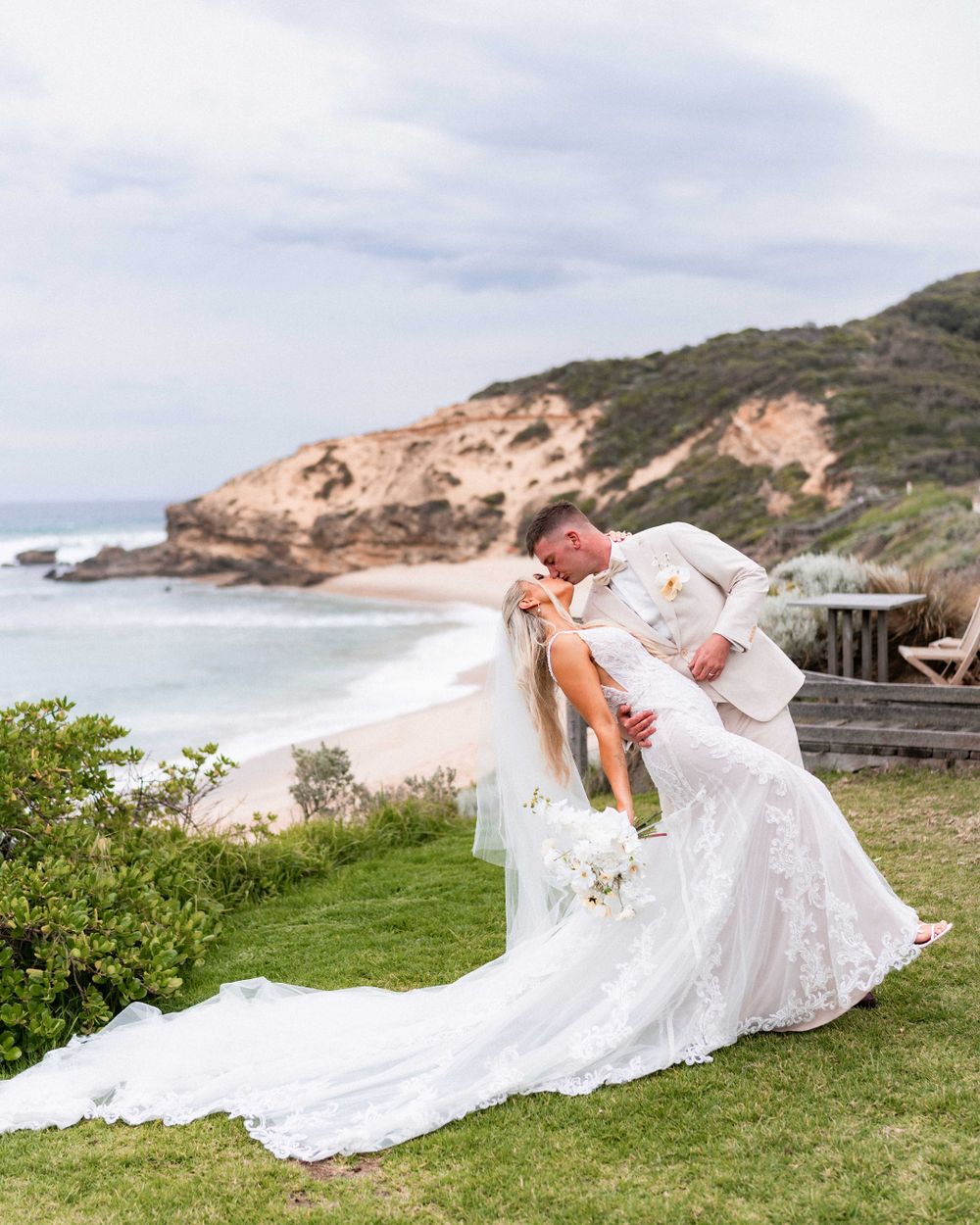 A flowing white wedding dress billows dramatically against a coastal landscape with cliffs and ocean views.