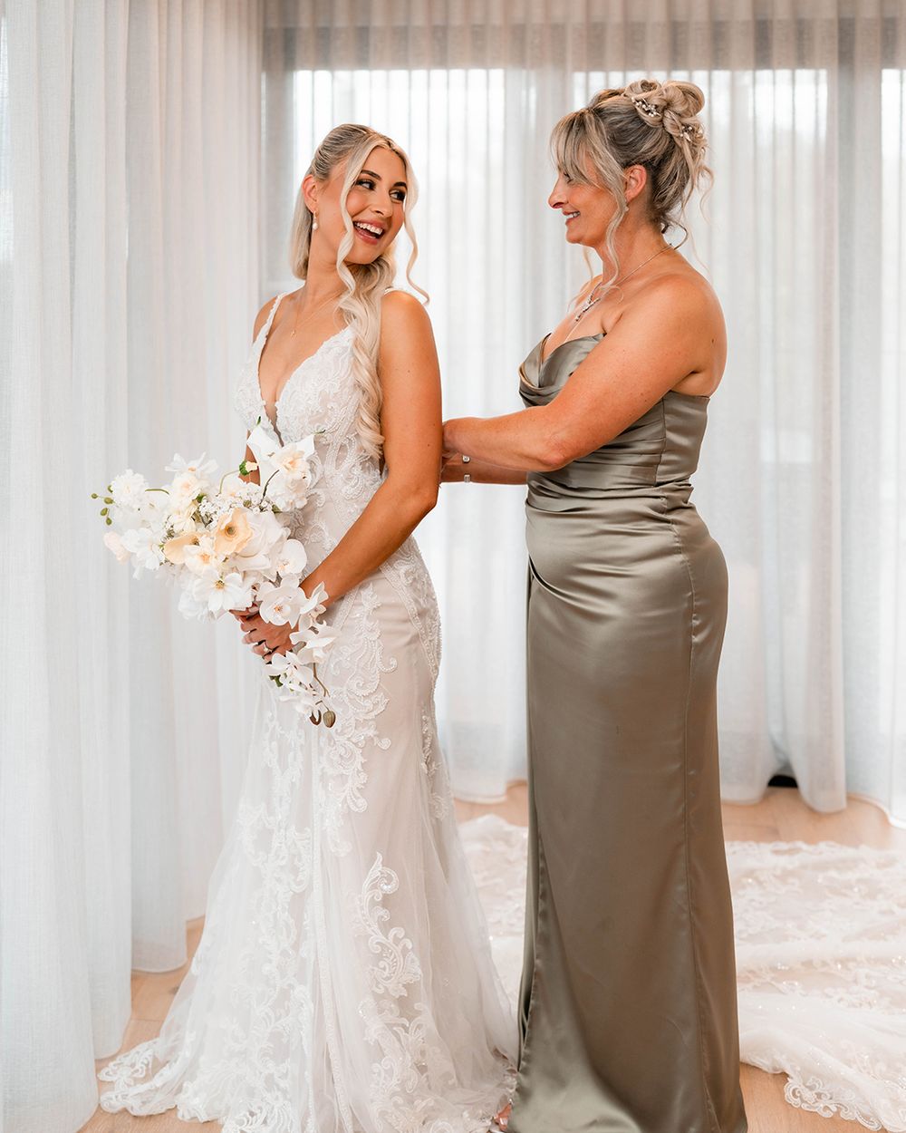 Two people share a joyful moment in formal attire, with a white lace wedding gown and champagne silk dress.