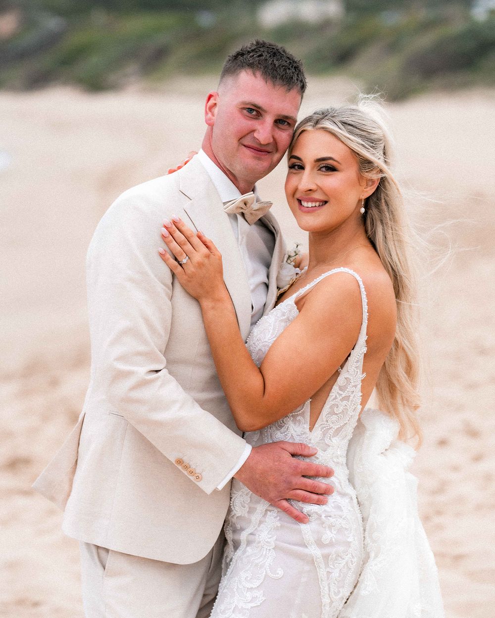 A romantic couple shares intimate moments in white attire during a beach photoshoot at sunset.