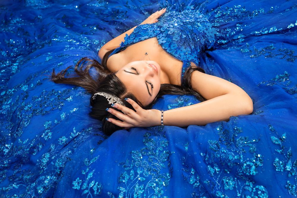 A person lies on a vibrant blue textile surface in an artistic pose with dramatic lighting and shadows.
