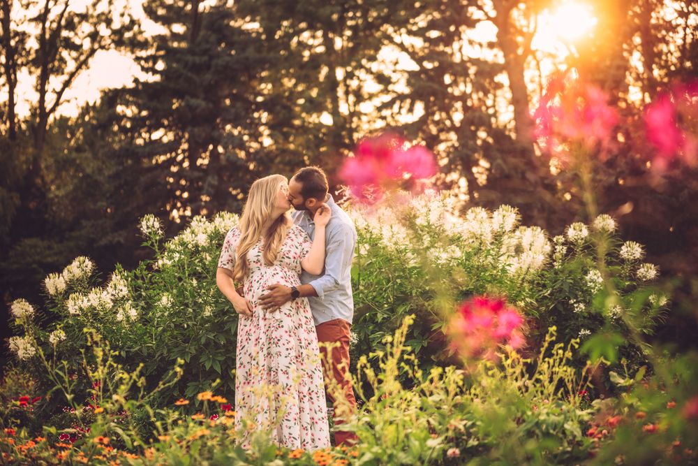 Romantic couple embraces in a wildflower garden during golden sunset with lens flares and pink blooms.