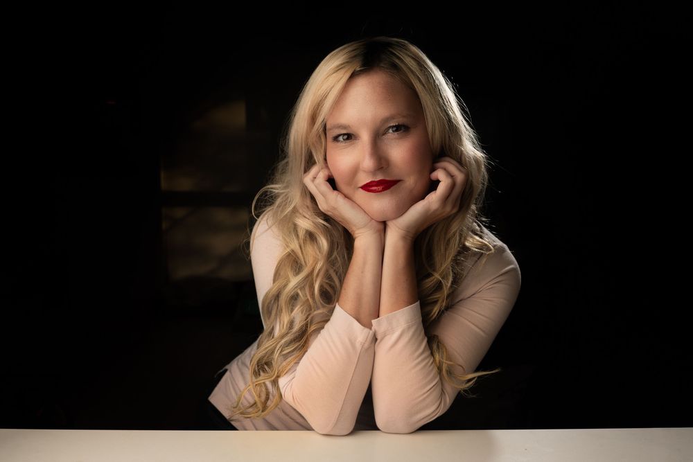 Professional studio portrait of someone in a beige sweater against a dark background with dramatic lighting.