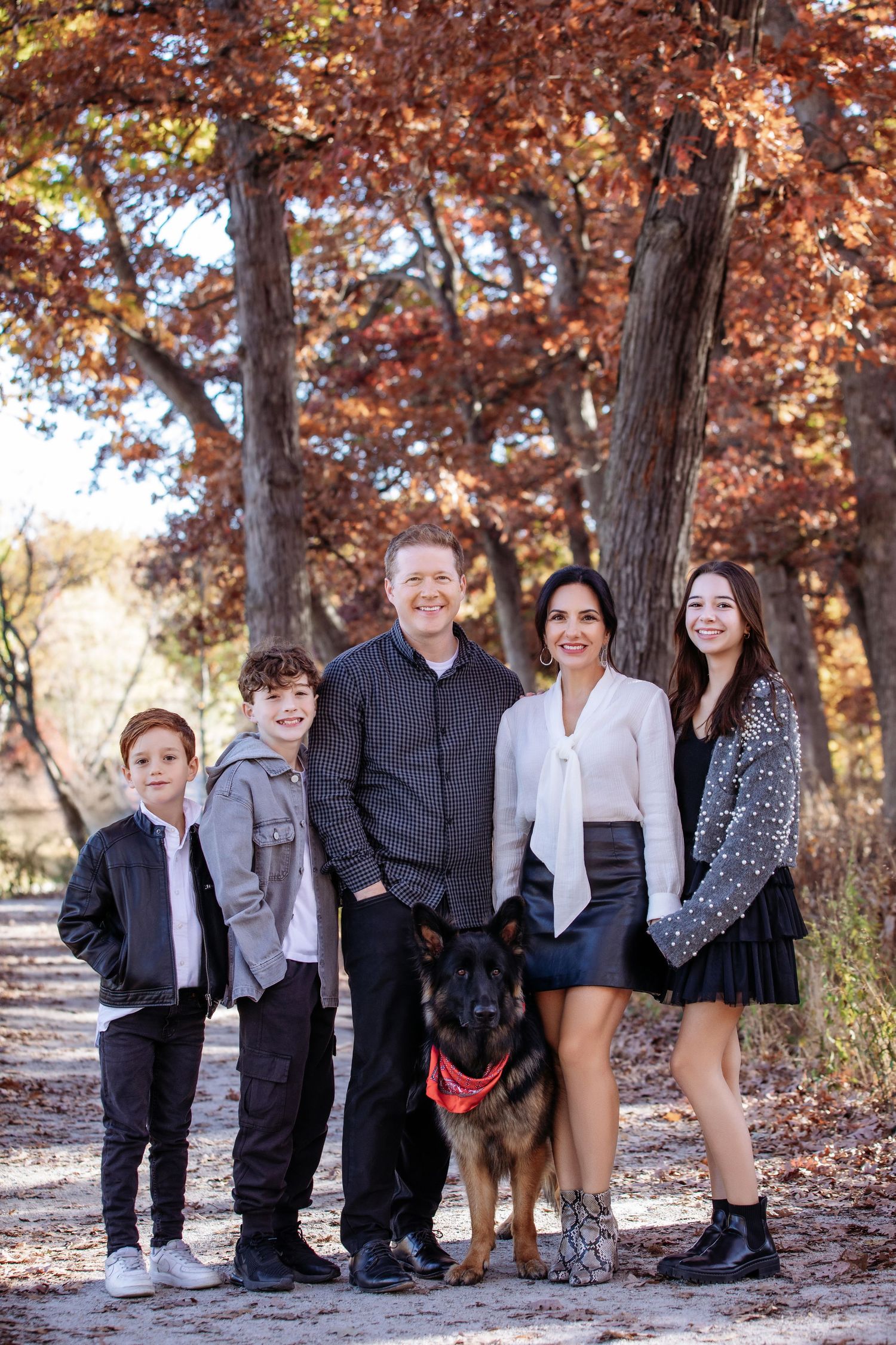 Family fall photo session with German Shepherd dog posing on autumn trail with colorful fall foliage.