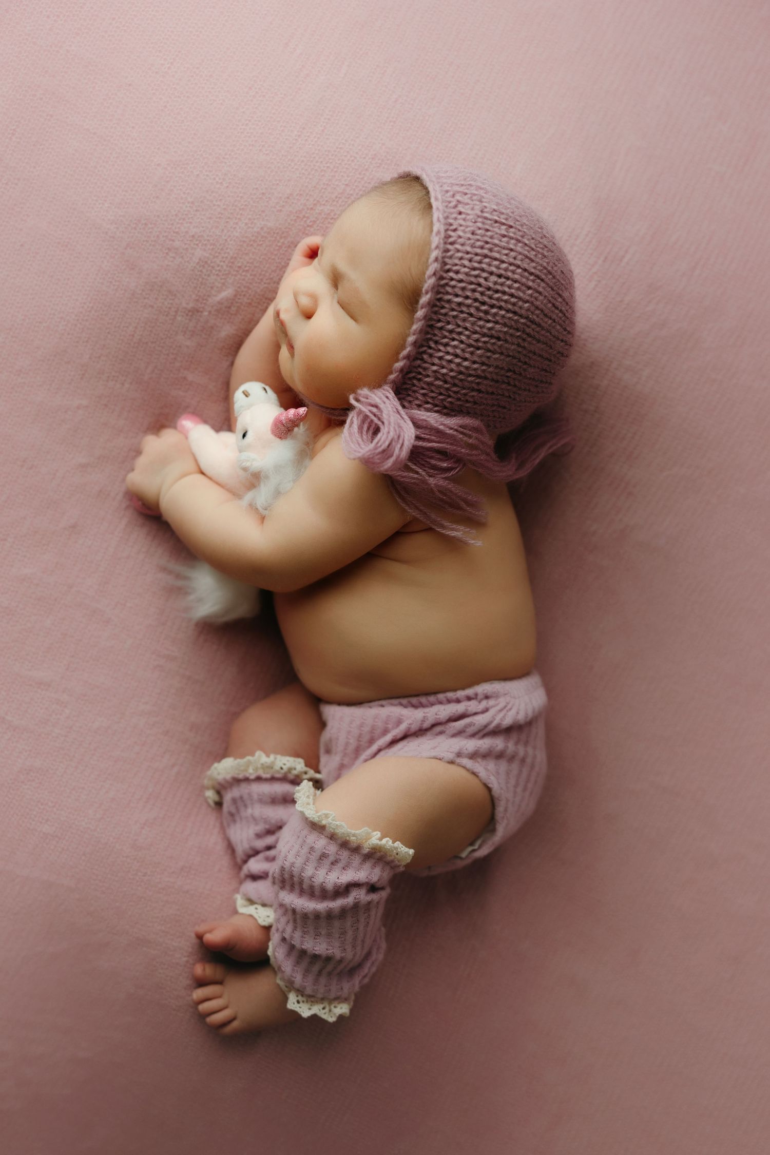 Sleeping newborn baby in pink cuddling a white stuffed bunny on a pink backdrop at the newborn photo studio in victoria bc.