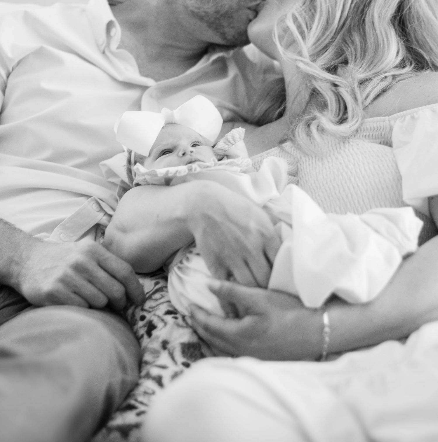 Black and white intimate portrait of parents cuddling with their newborn baby.
