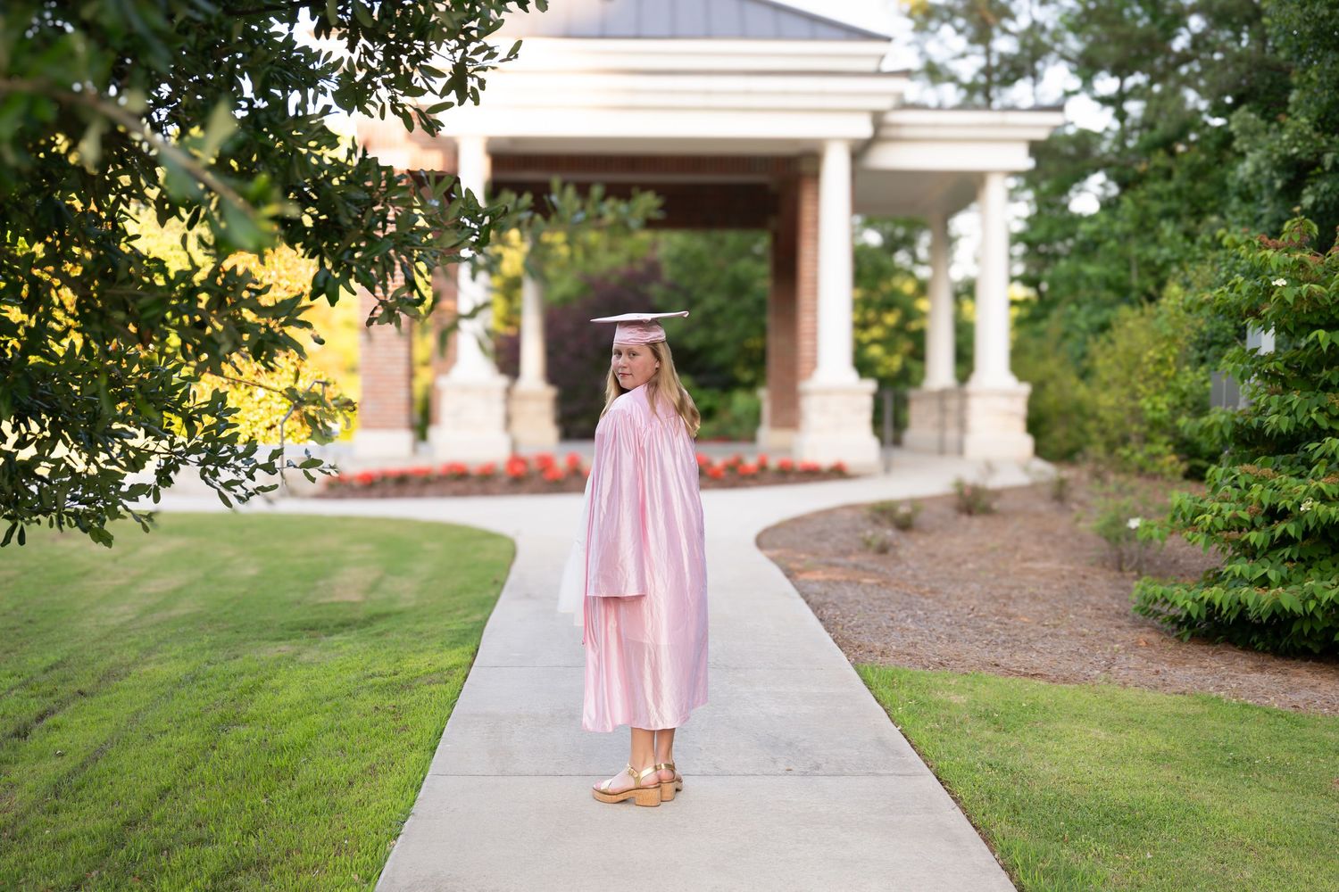 Young child in a pink dress walks along a concrete path outside a residential home.