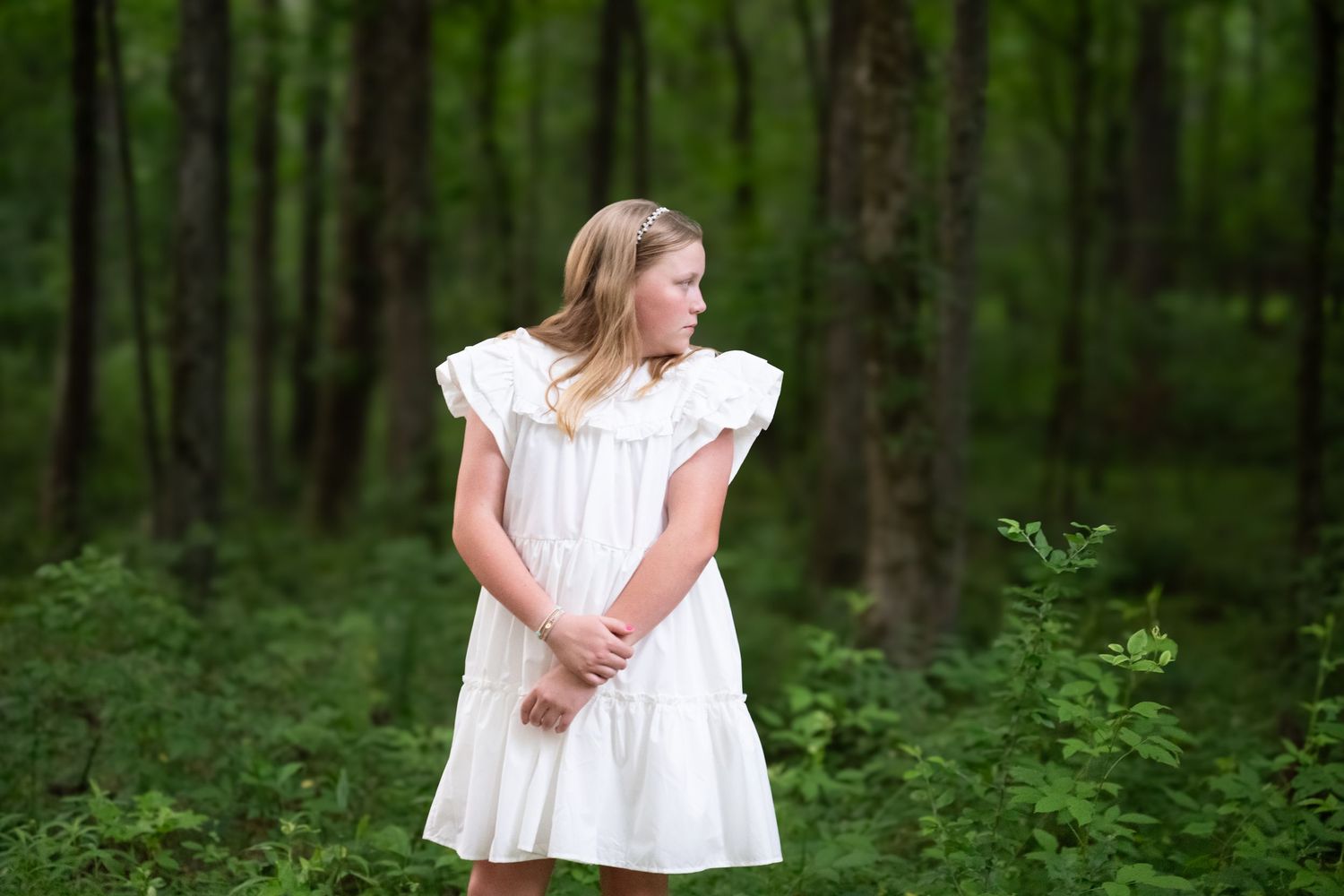 A white dress flows in a lush forest setting during a portrait session.