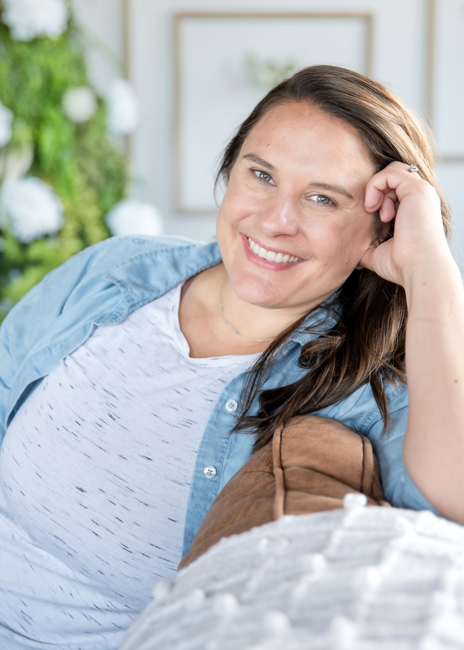 Woman in chambray shirt relaxing on couch with greenery in background.