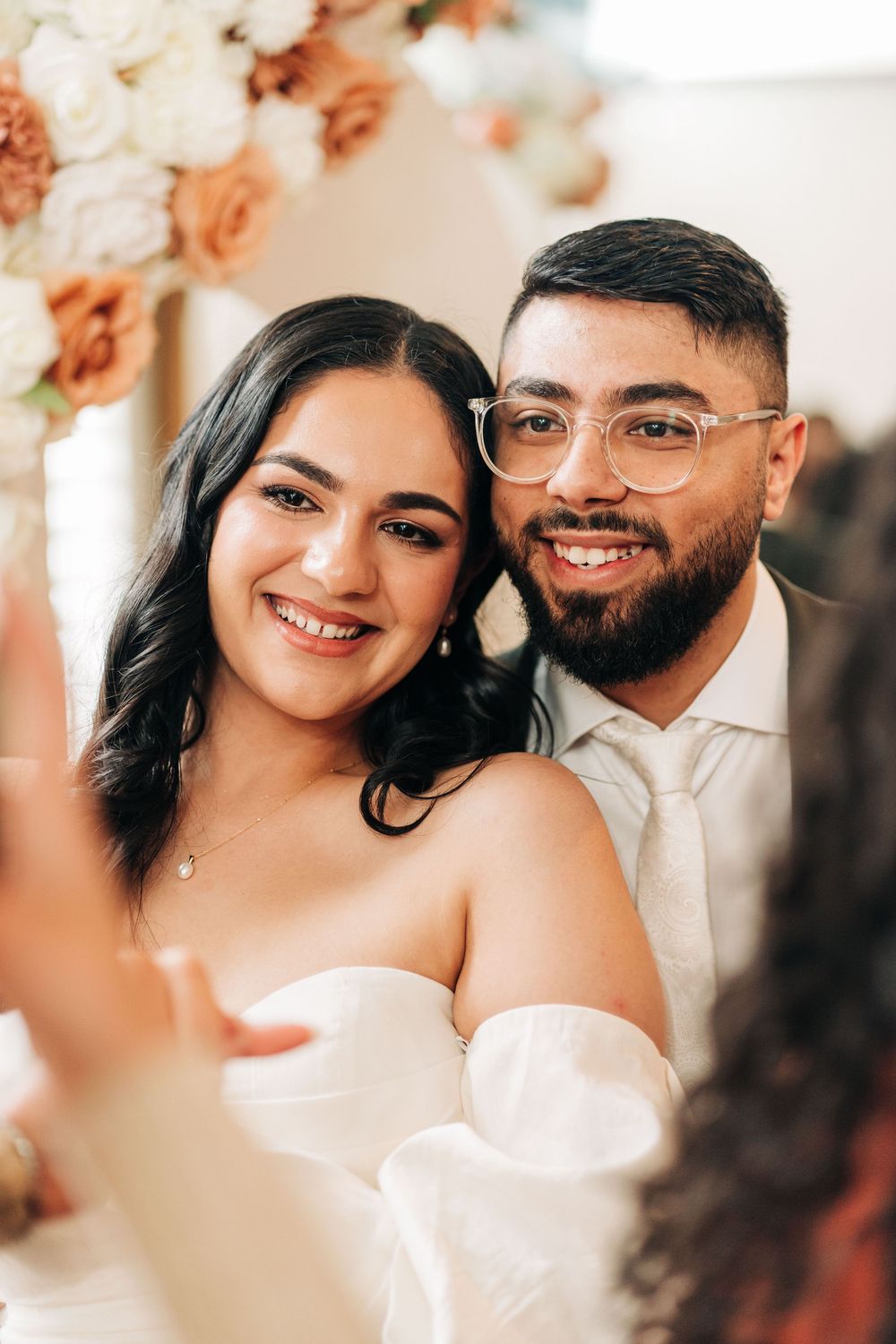 Smiling bride and groom posing together at their wedding ceremony with floral arch backdrop.