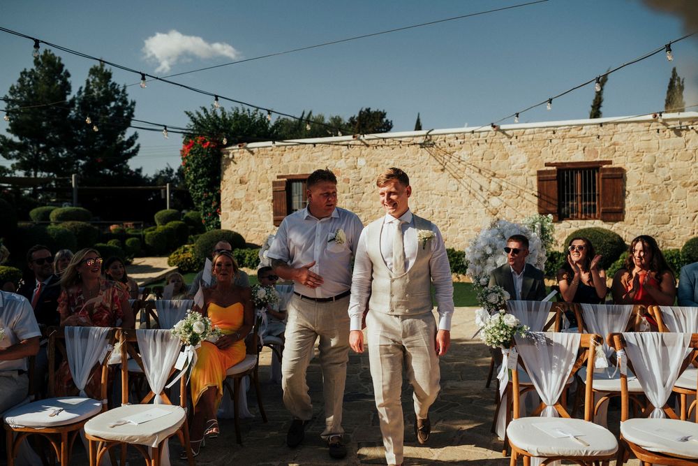 Wedding guests gather at an outdoor reception venue with stone walls and string lights at dusk.