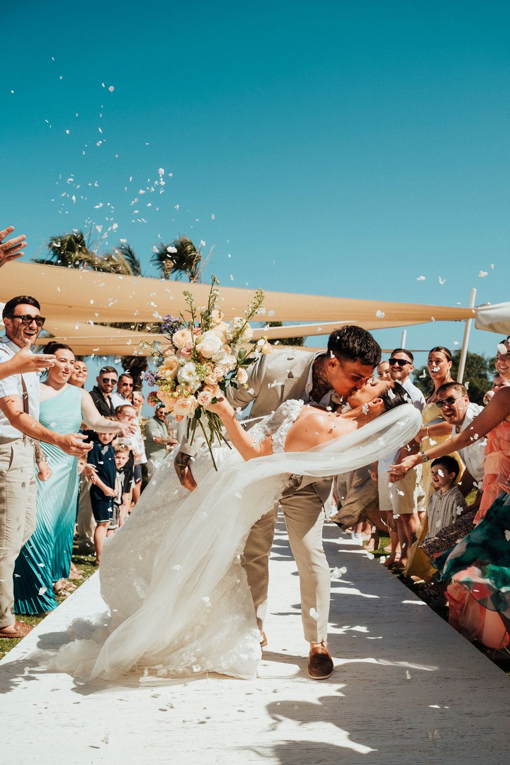 Wedding party celebrates on a sunny beach with confetti and flowing white dress creating a joyful atmosphere.