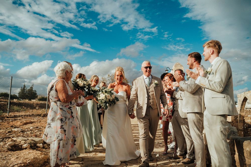 Wedding party in light colored attire poses together on a beach during sunset with dramatic blue sky overhead.