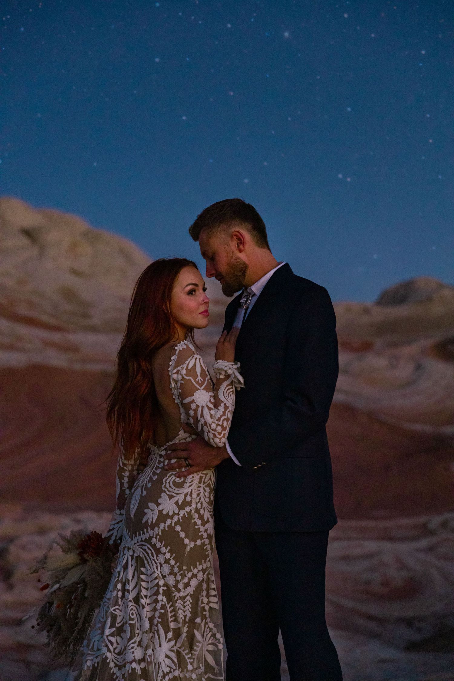 Romantic nighttime desert photoshoot under starry sky with red rock formations.