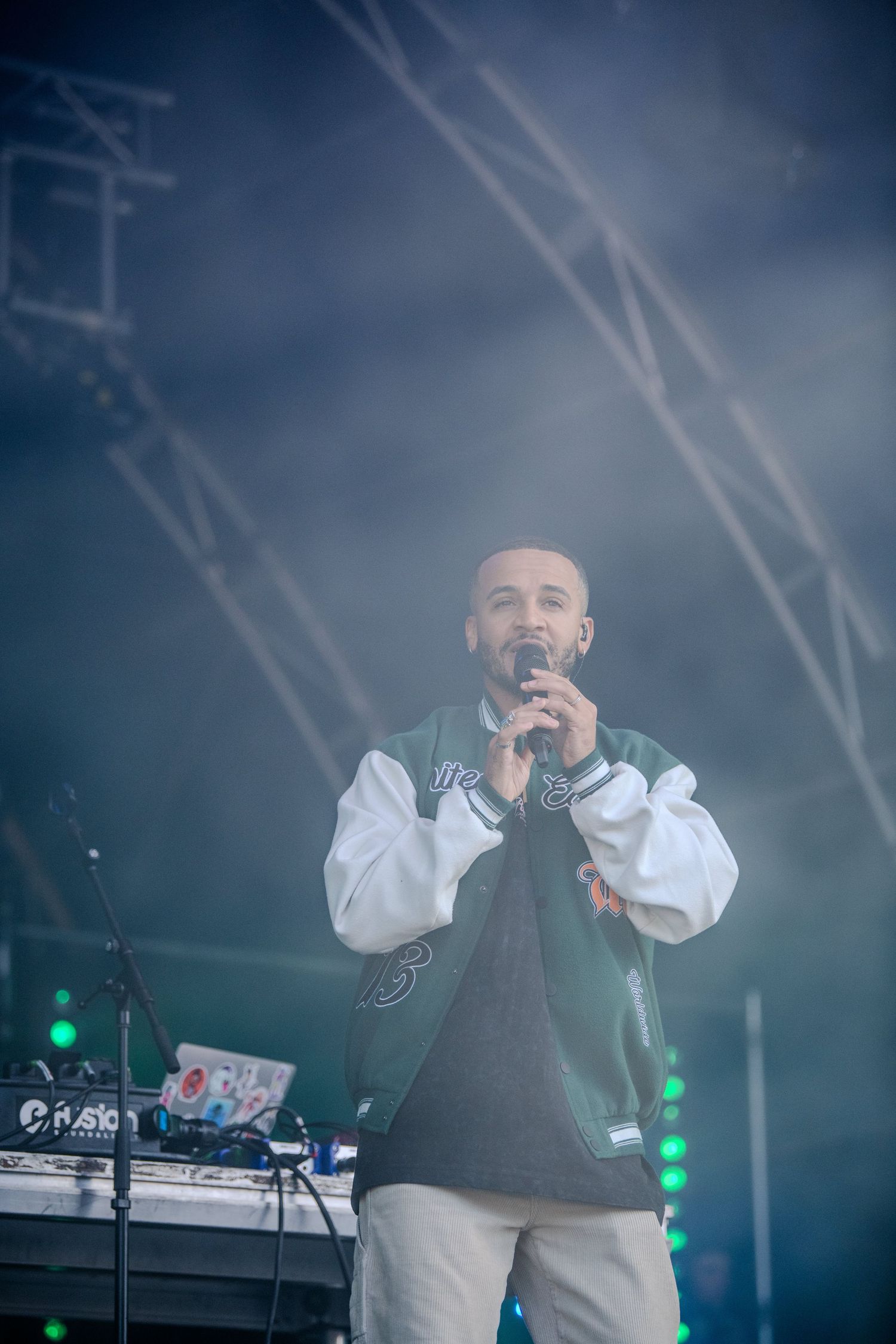 Singer performs on stage in a white shirt and dark vest against atmospheric lighting.