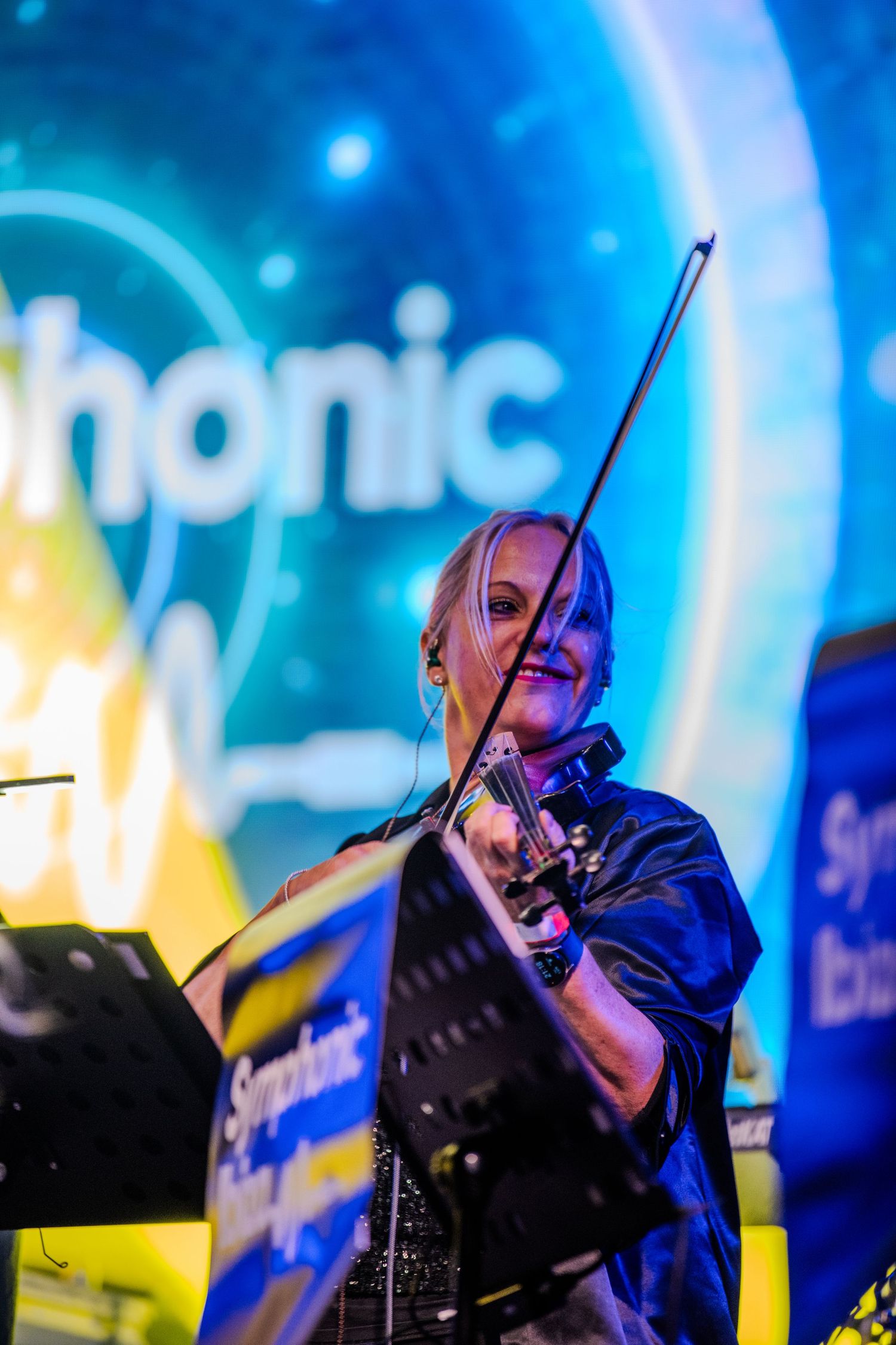 Performer playing violin in dramatic blue stage lighting during live musical performance.