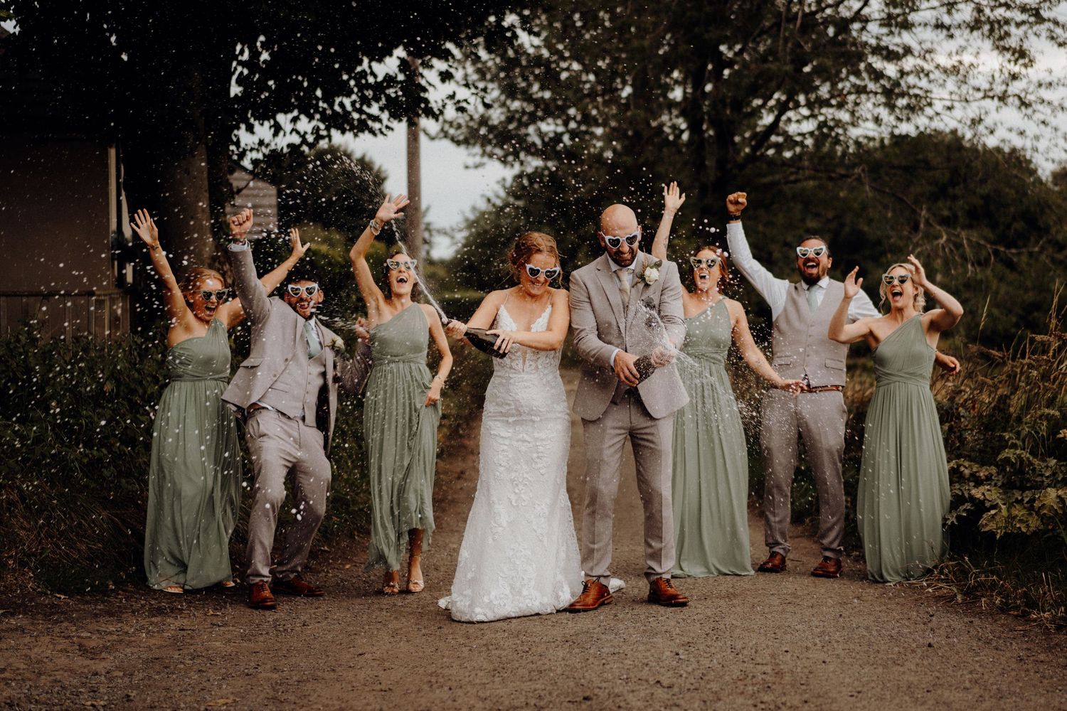 Wedding party in sage green and neutral dresses pose together in a garden setting during golden hour.