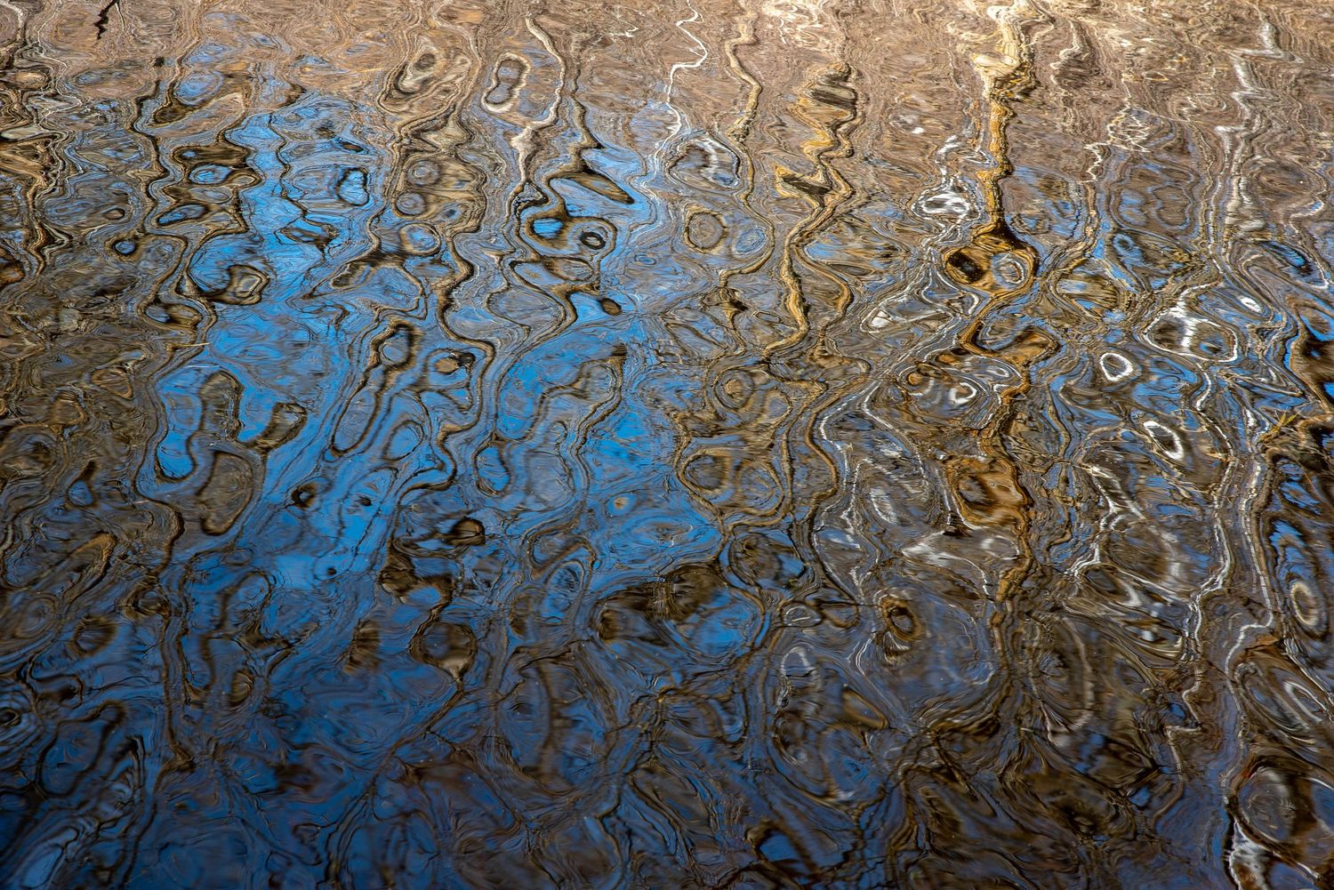 Abstract water reflection creating blue and brown wavy patterns.