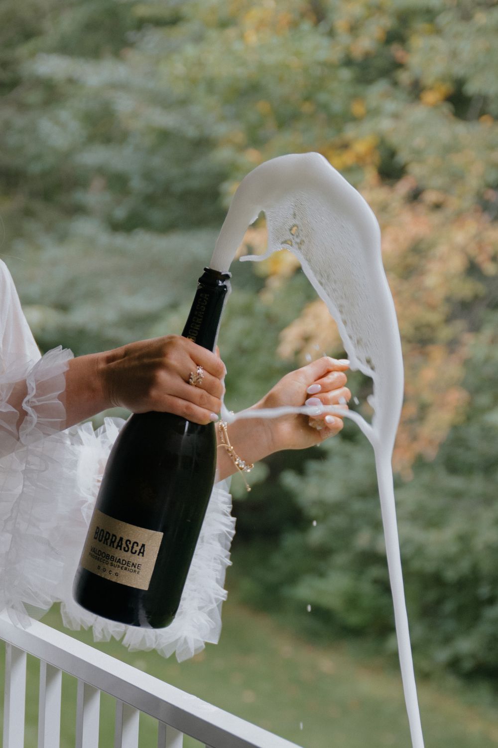 Champagne bottle being popped in sequence showing cork and foam spraying against a green outdoor background.