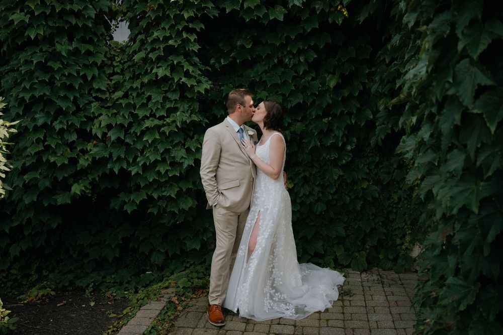 A romantic outdoor wedding moment against a lush green wall of ivy on a stone walkway.
