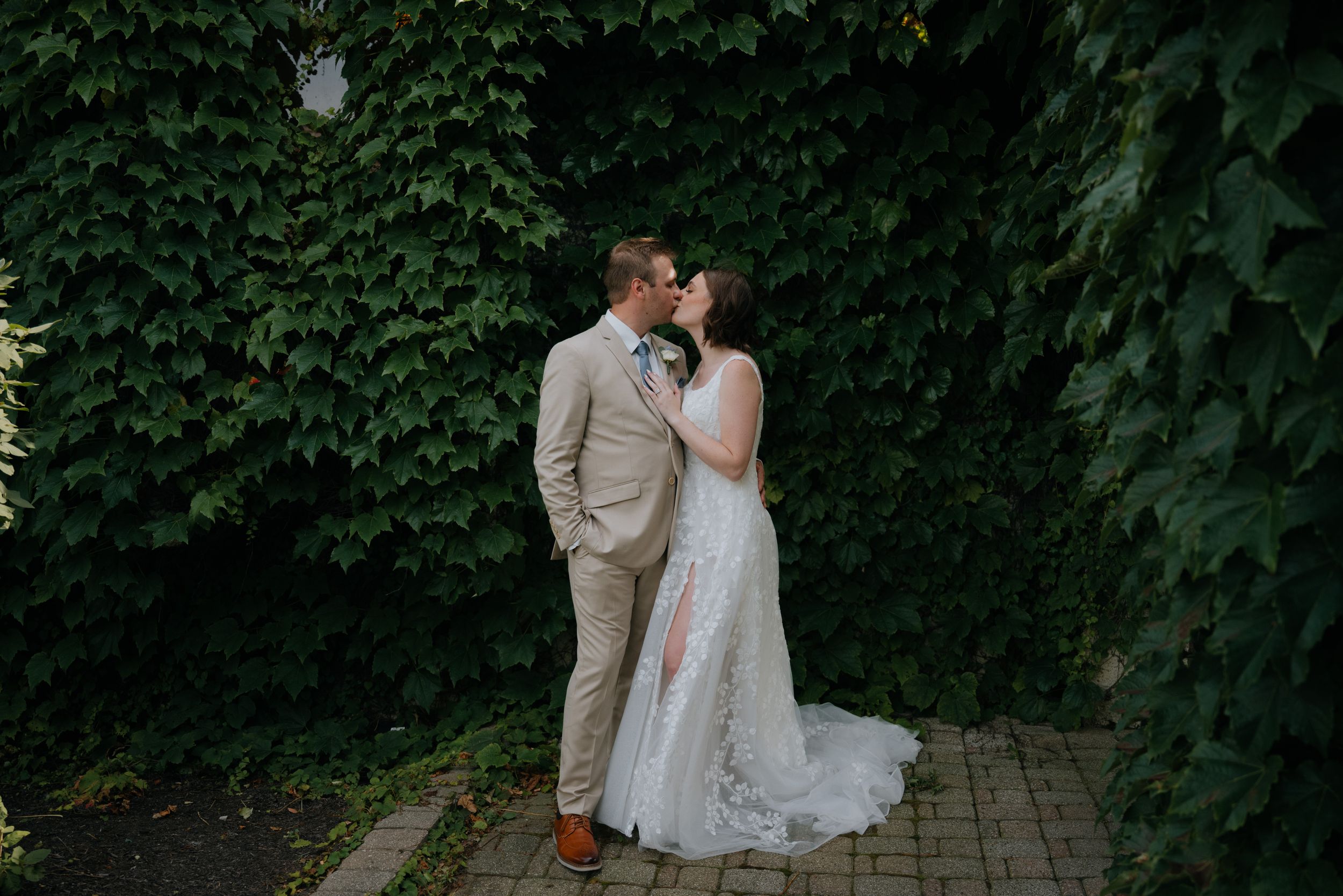 A romantic outdoor wedding moment against a lush green wall of ivy on a stone walkway.
