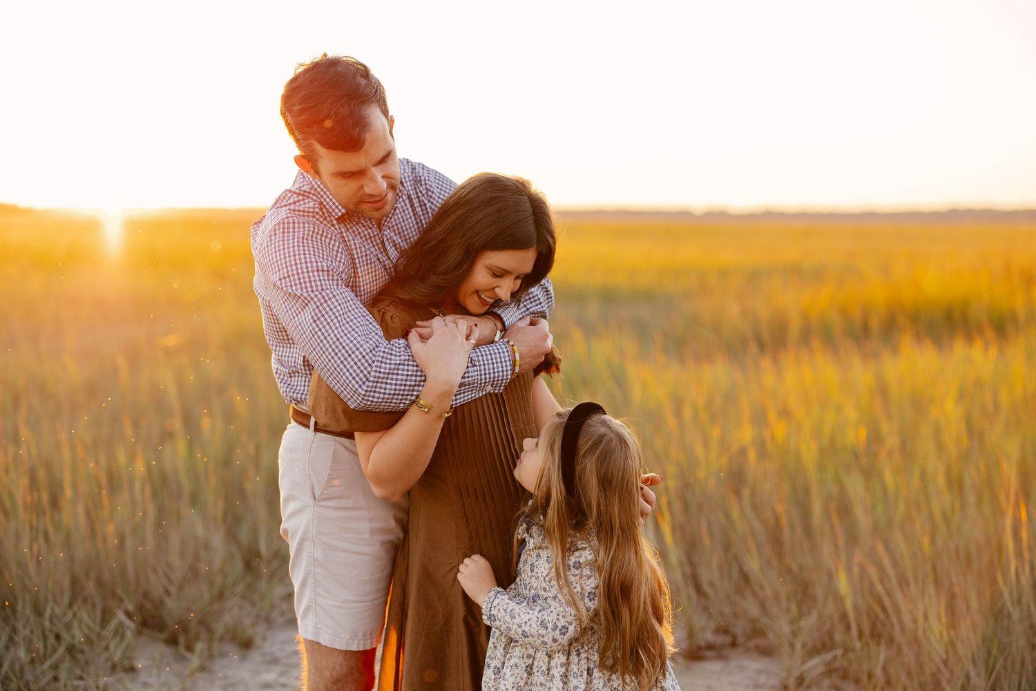 A joyful outdoor family moment captured beneath sun-dappled trees on a pathway.