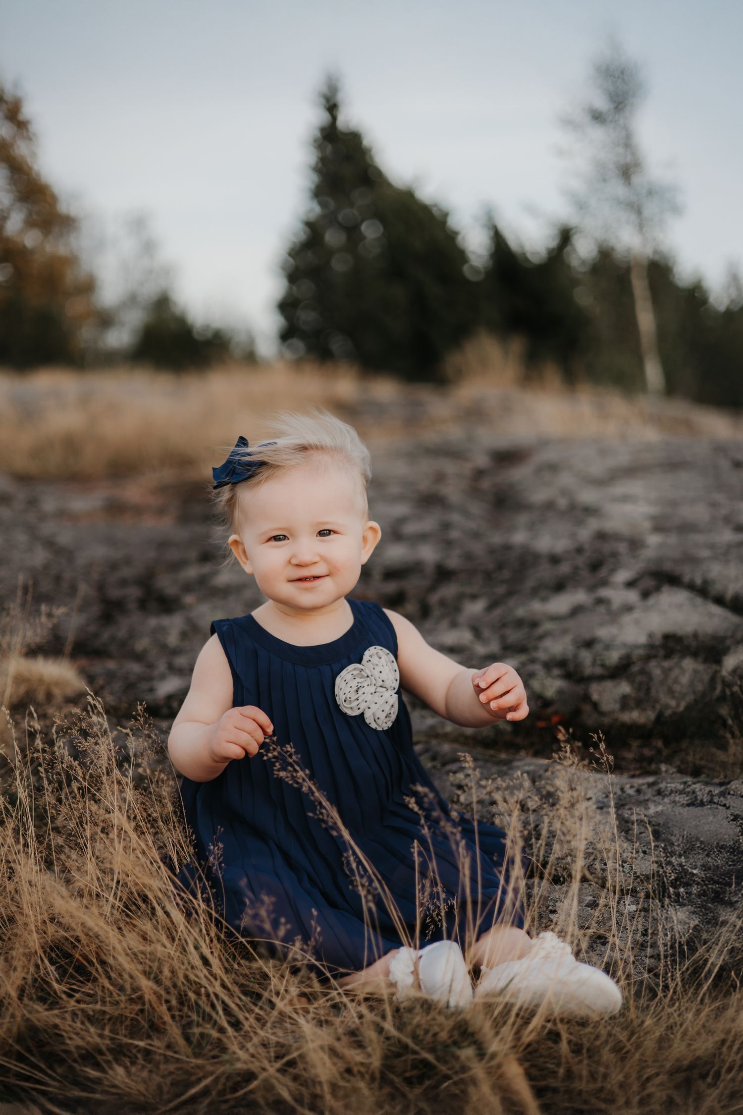 Baby in white romper sitting on floor during indoor photo session.
