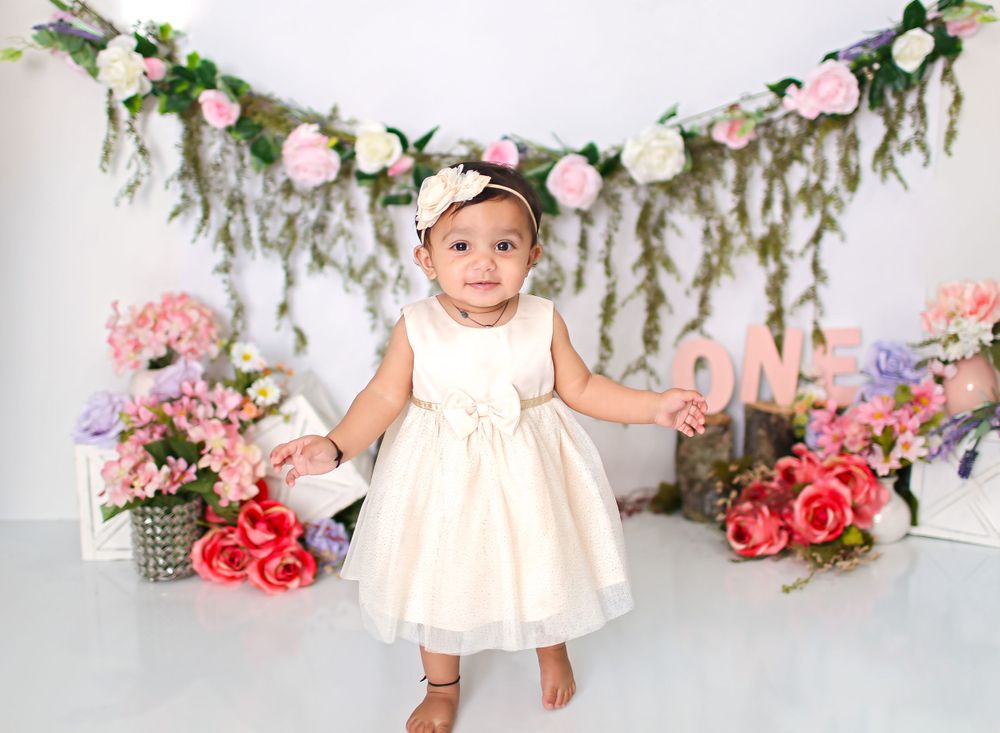 First birthday session with little girl in white dress with garland on wall and flowers