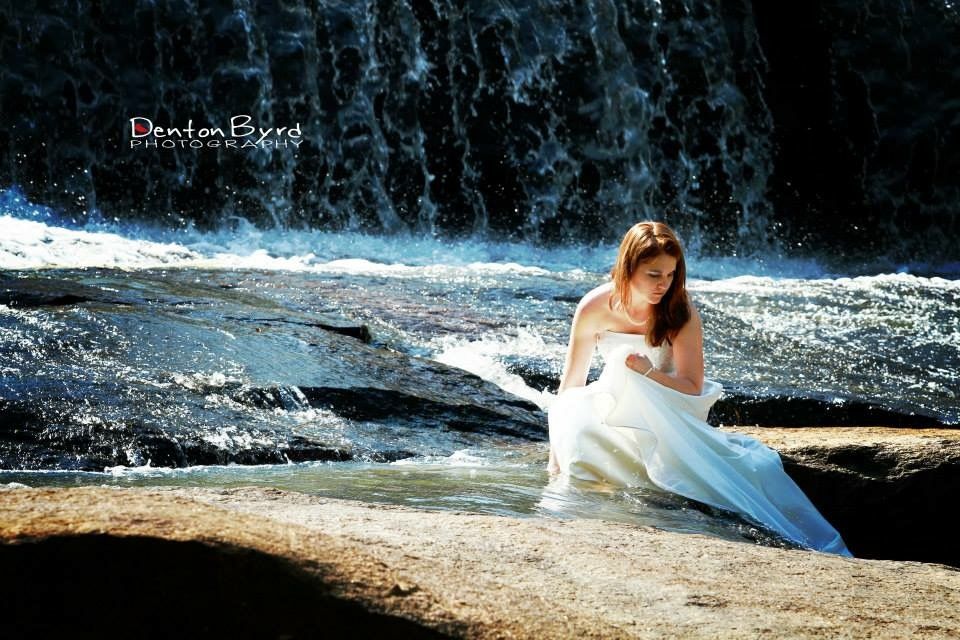 A woman in a white dress poses near a cascading waterfall.