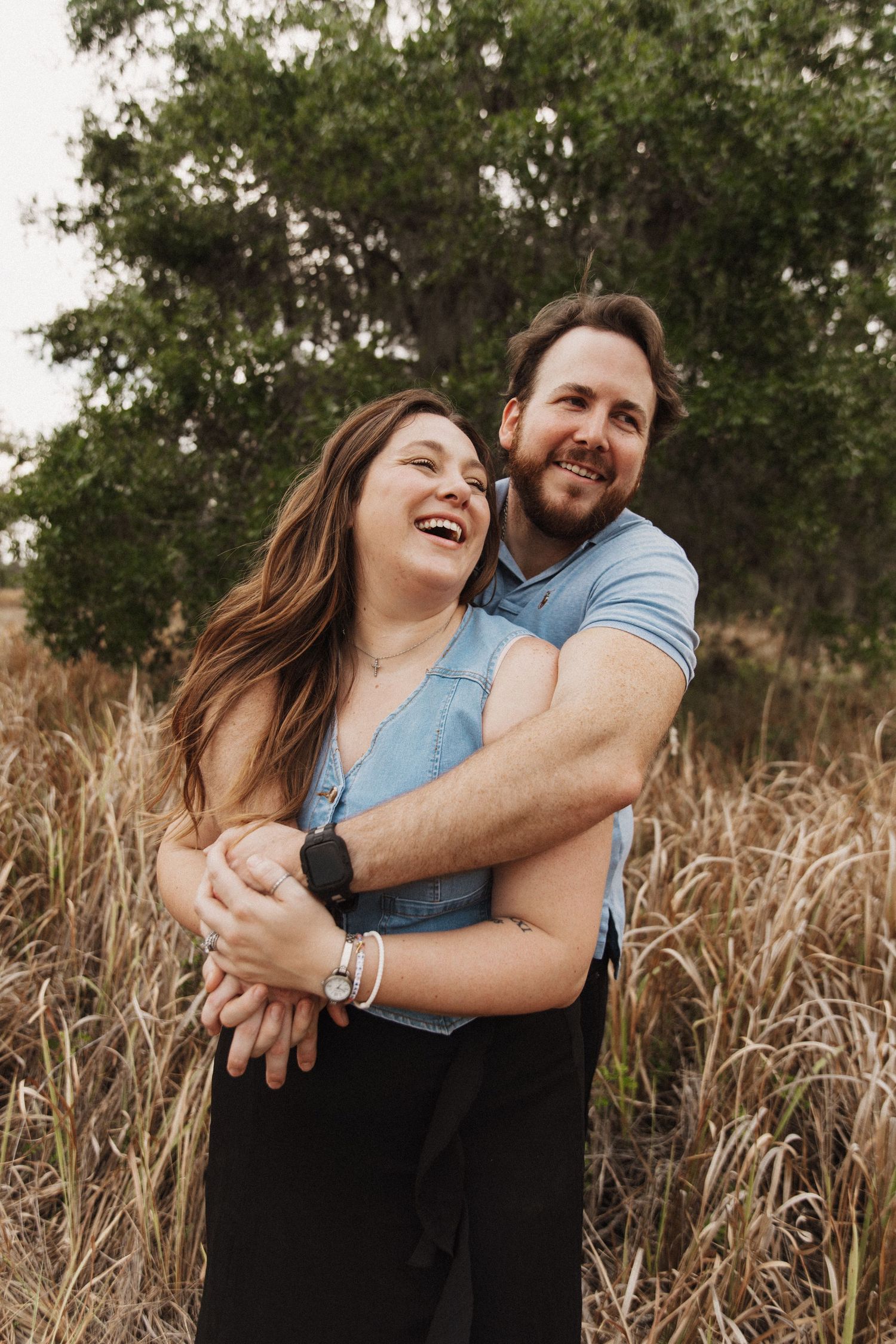 Couple embracing outdoors in autumn field, with person wearing vibrant orange dress.