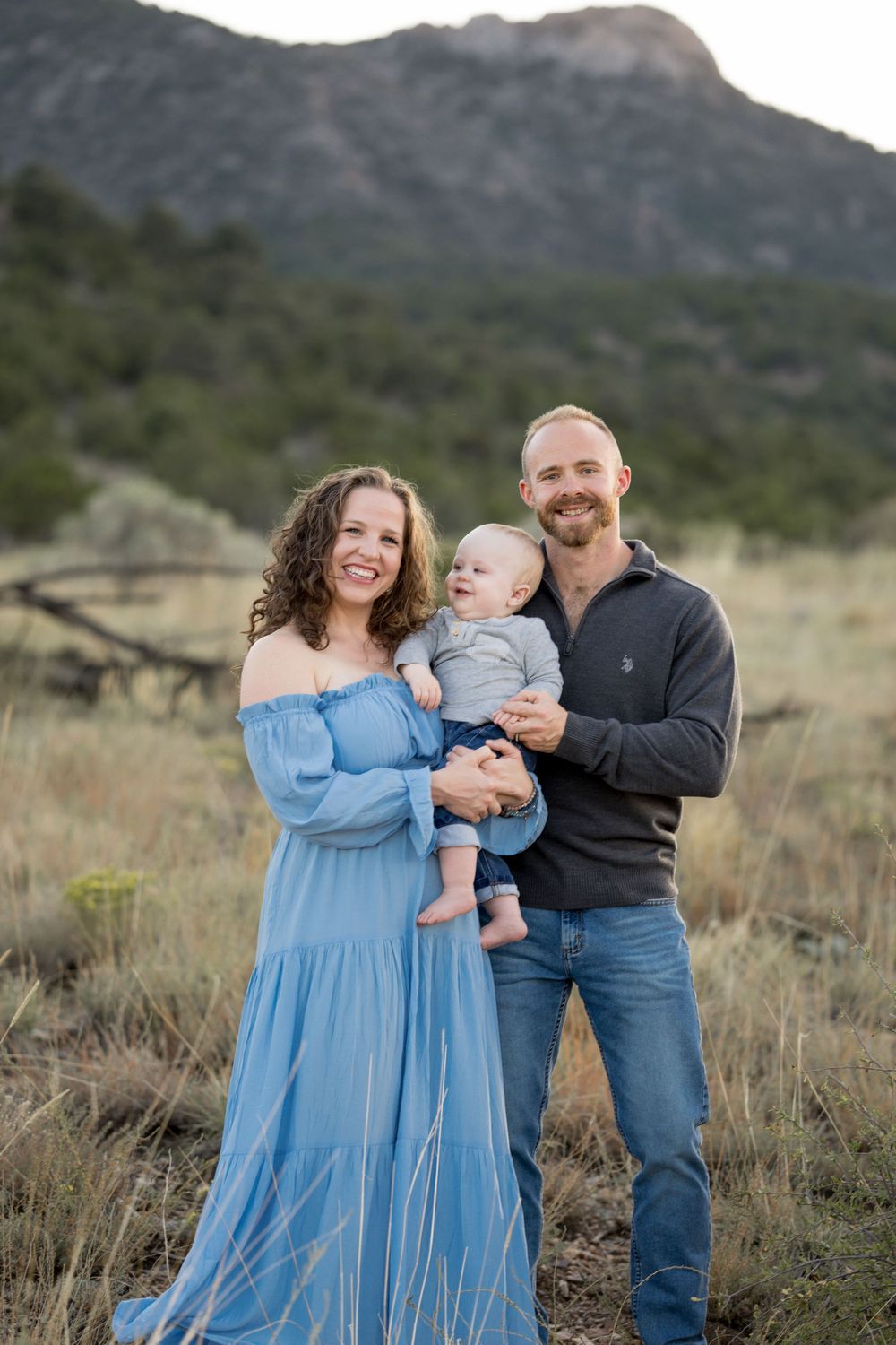 A family shares tender moments together in a mountain field at sunset while wearing blue and denim.
