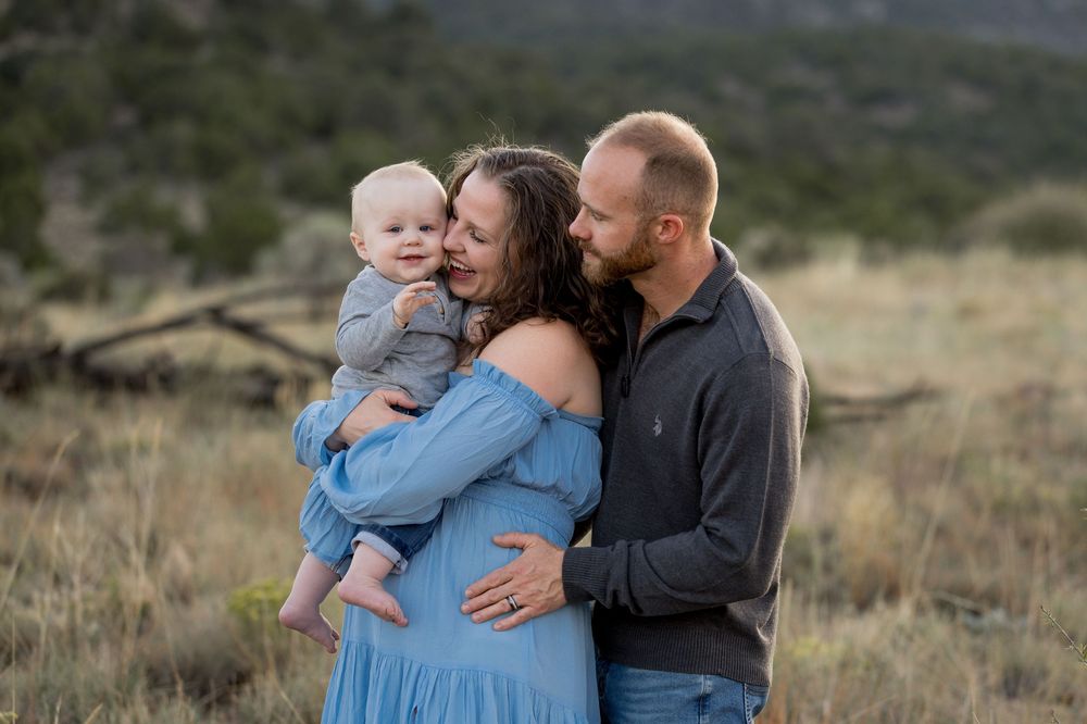 A family shares a tender moment together in a natural outdoor setting with mountains in the background.