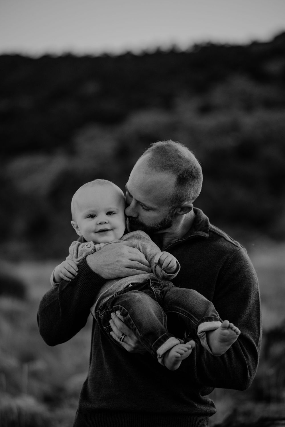 A series of black and white photos showing tender moments between a parent and baby in an outdoor setting.