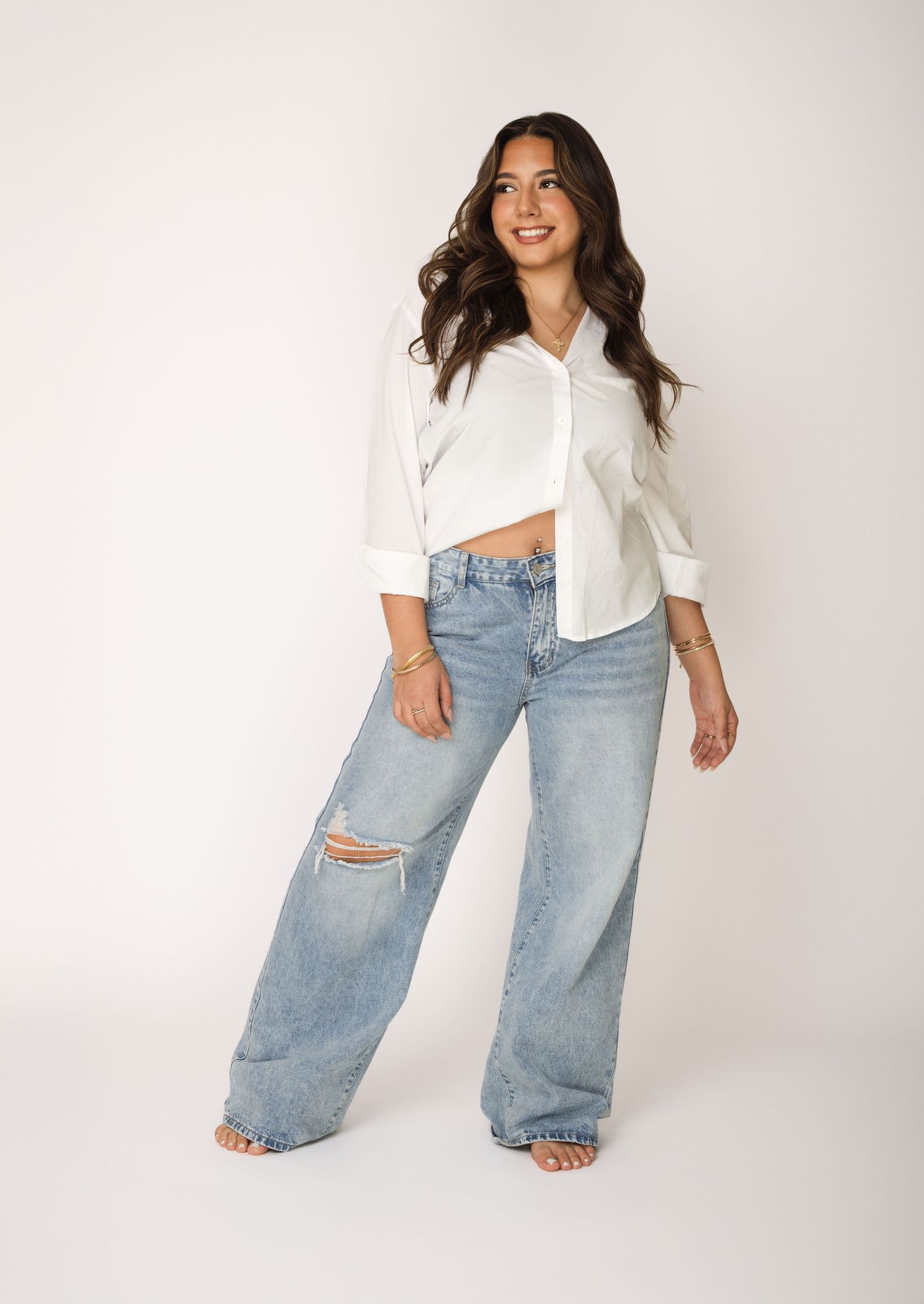 A model in a white cropped button-down shirt and distressed wide-leg jeans poses against a light white backdrop.