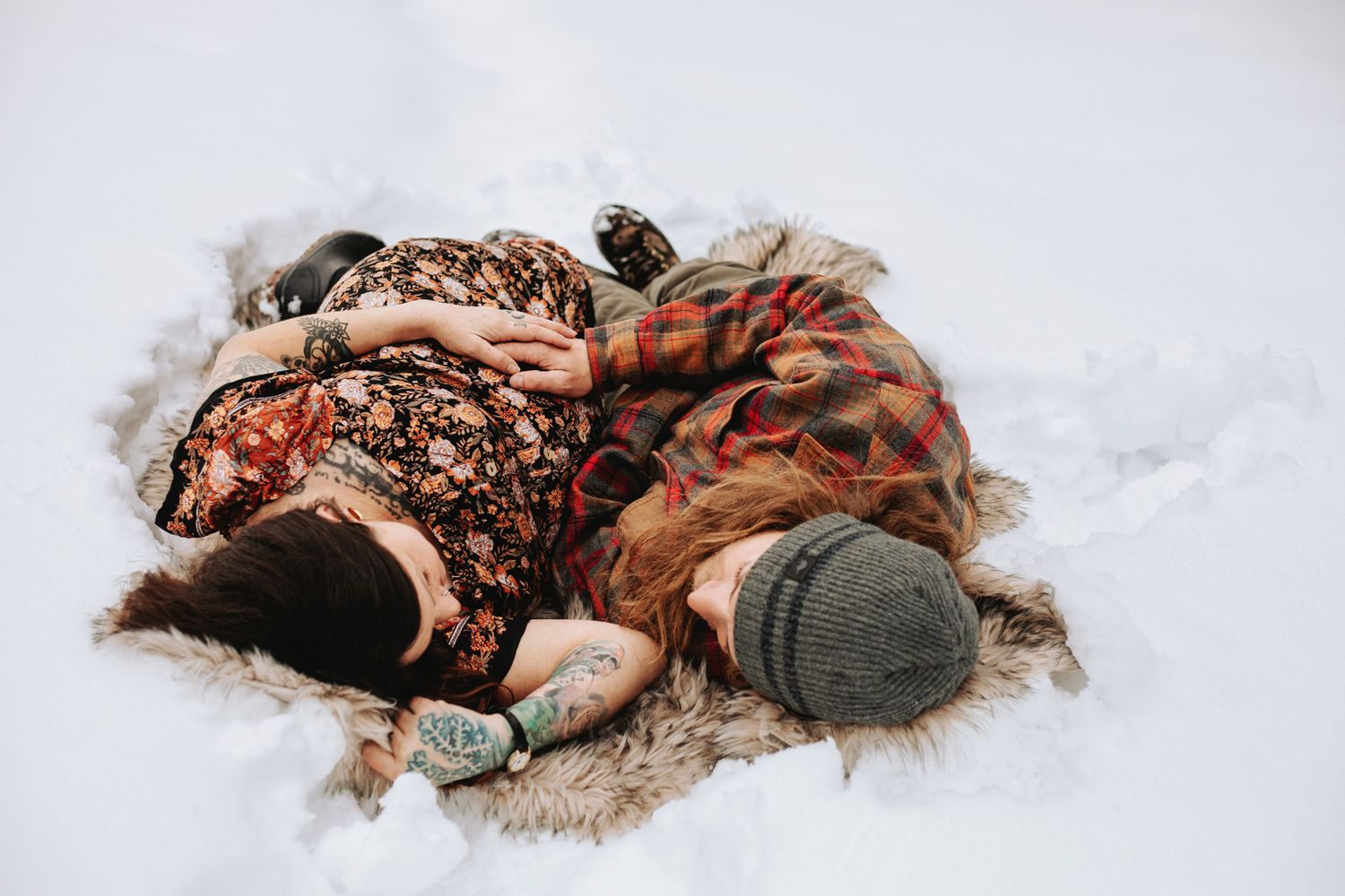 pregnant woman and her partner lay on a fur blanket in the snow during a maternity photography session in Lake Tahoe