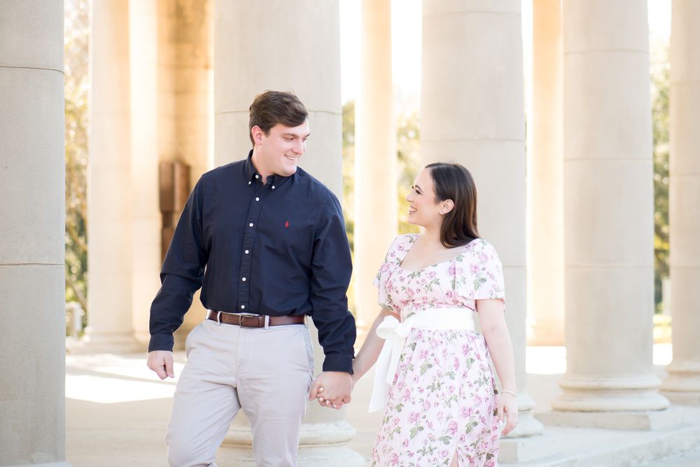 Romantic couple poses together in a white columned walkway with natural lighting.