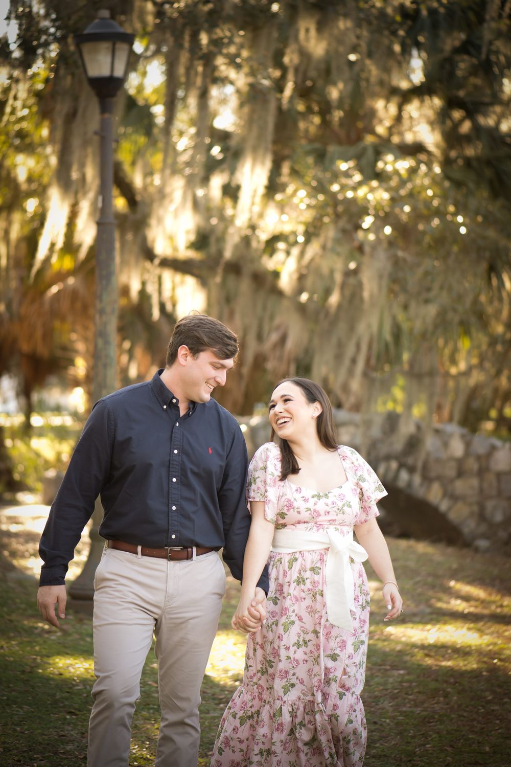Couple walking and laughing together under moss-covered trees in afternoon light.