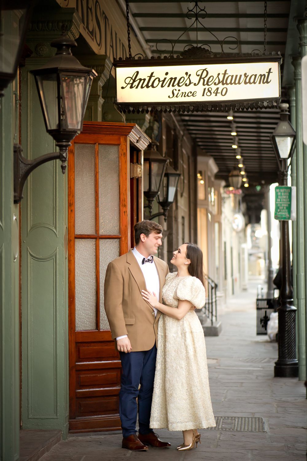 Couple poses for romantic photos along a covered walkway with green columns and wooden doors.