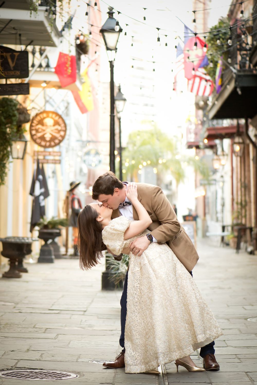 Romantic dance poses on a historic street with flags and decorative lighting.