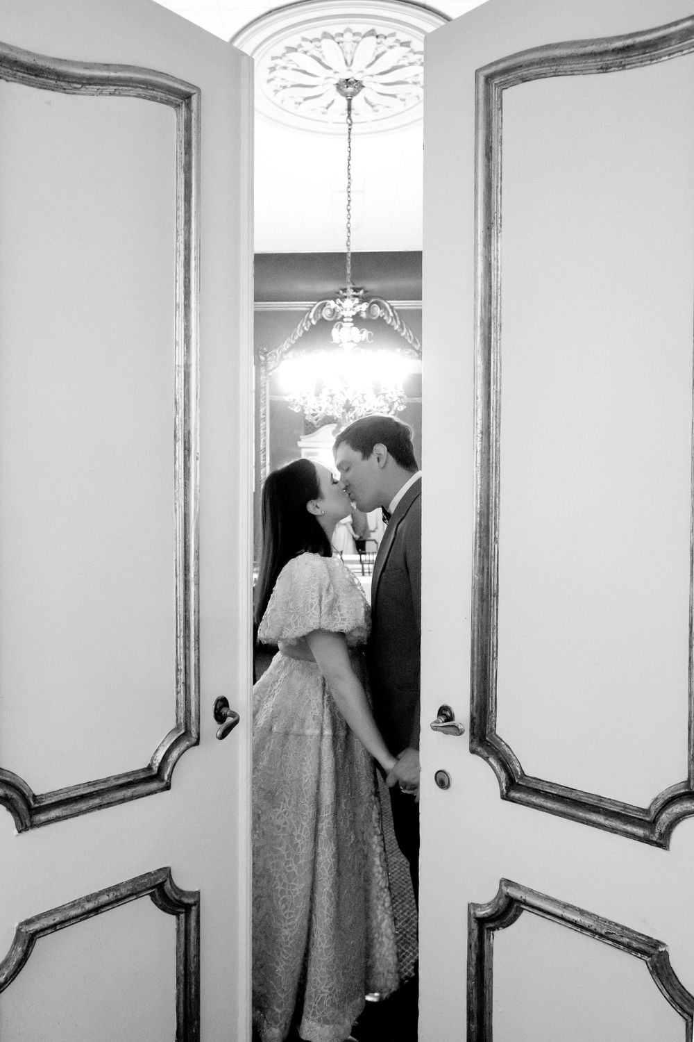 Black and white photos in an elegant hallway with ornate mirrors and chandelier.