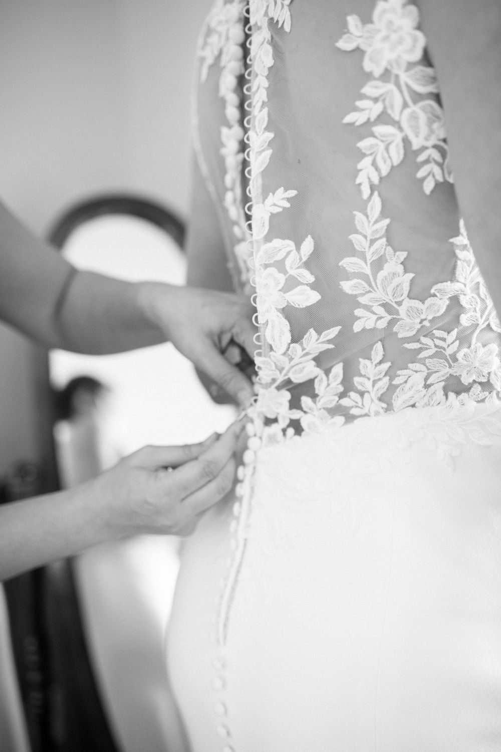 Maid of honor helping button wedding gown on bride