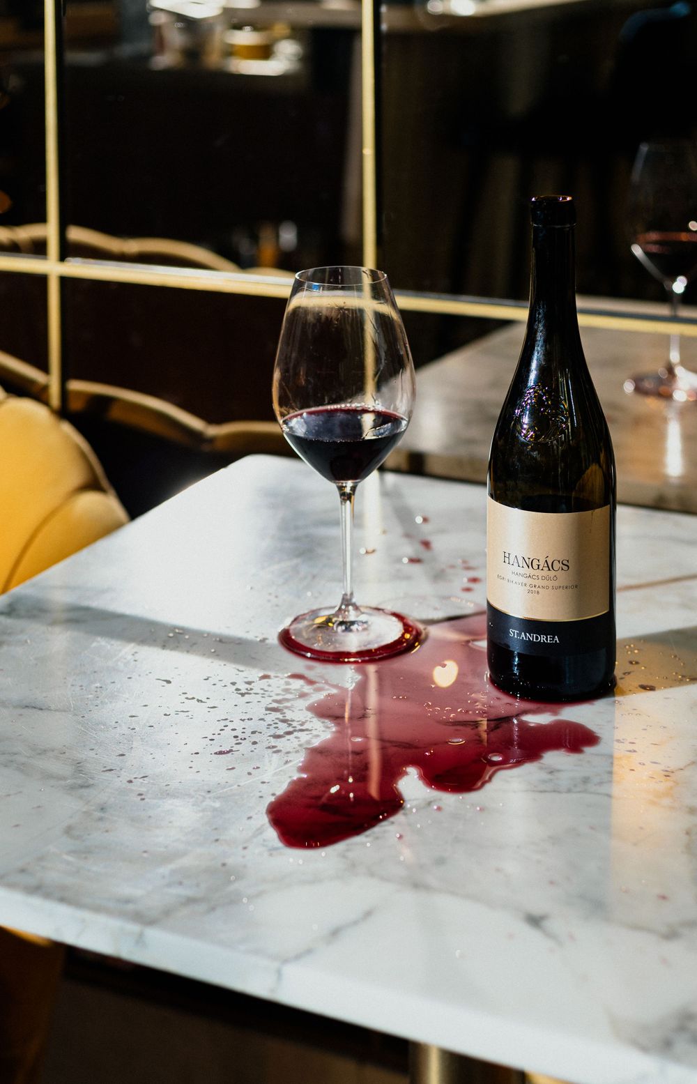 Red wine spilled on marble table with glass and bottle of Buscada wine.