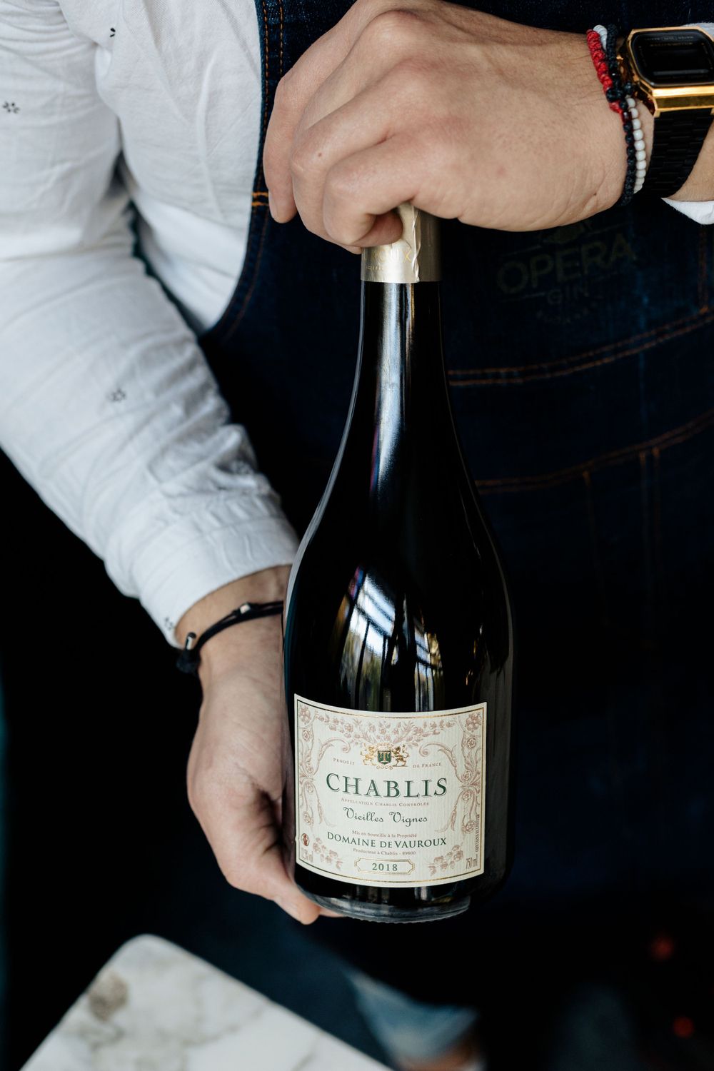 Hands holding bottle of Chablis wine against dark background.